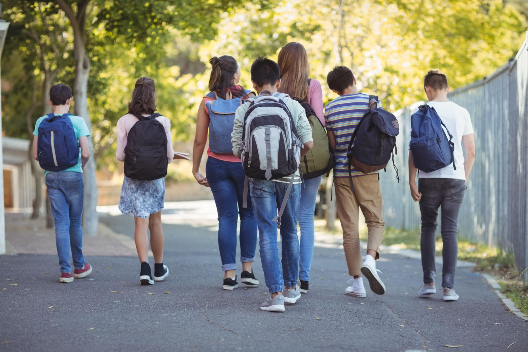 Copii și adolescenți cu ghiozdane mergând împreună spre școală