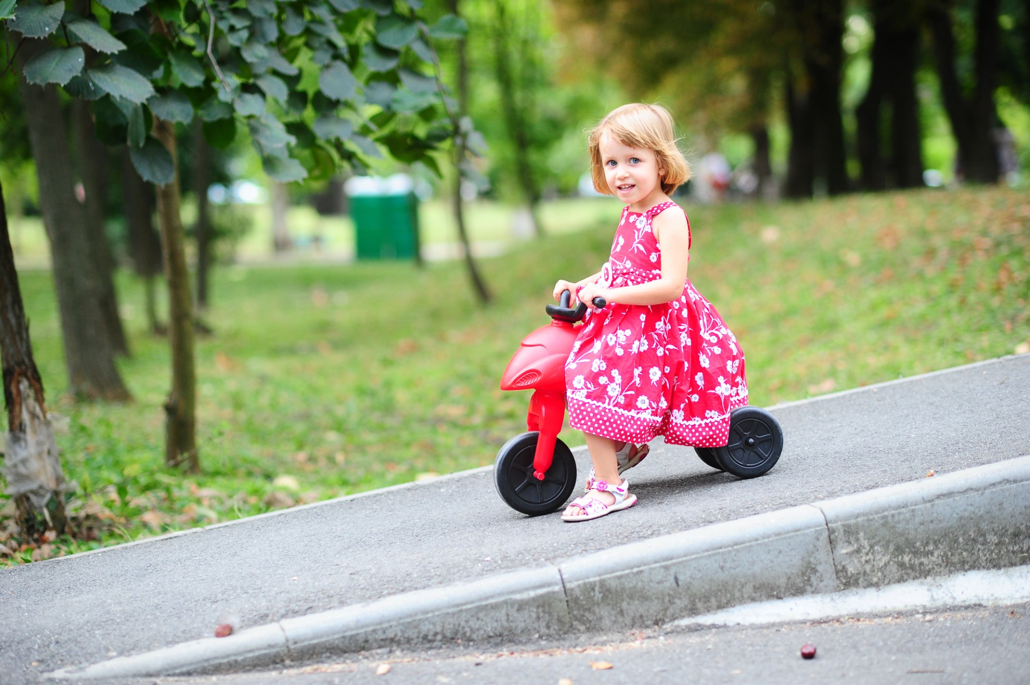 Un copil cu o tricicletă roșie într-un parc